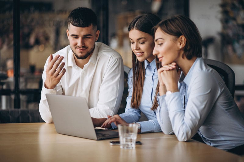 Three colleagues at a table, working together on a laptop, fostering teamwork and communication to sort the query of customers and provide solutions while they contact us.